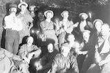 Black and white photo of mine workers inside a mine, some holding lit candles.