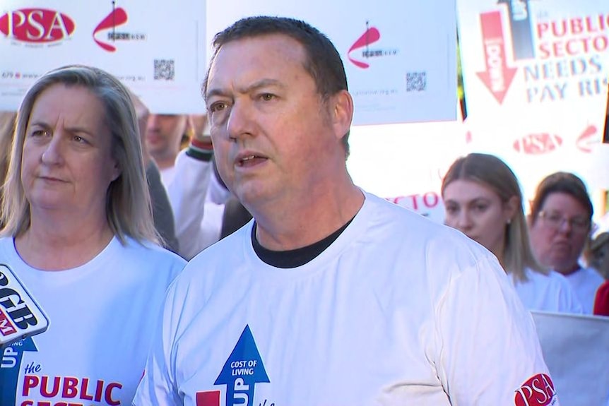 A man in a white t shirt standing in front of people holding placards.