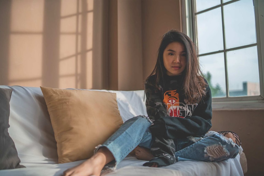 Woman wearing ripped jeans sitting on a couch and looking at the camera.