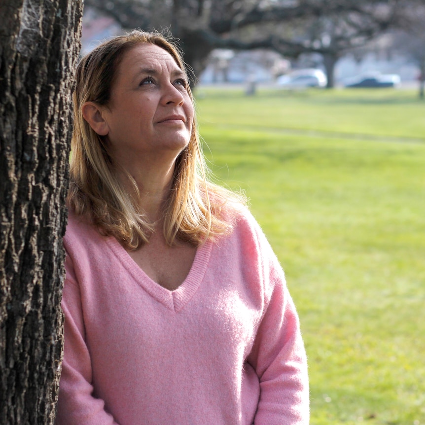 Kim Napier leaning against a tree in a park.