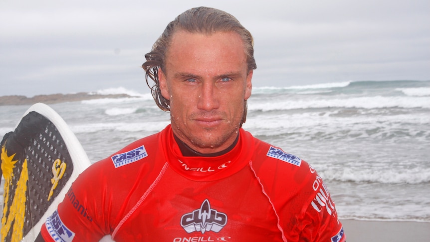 a surfer walking out of the ocean carrying a surfboard