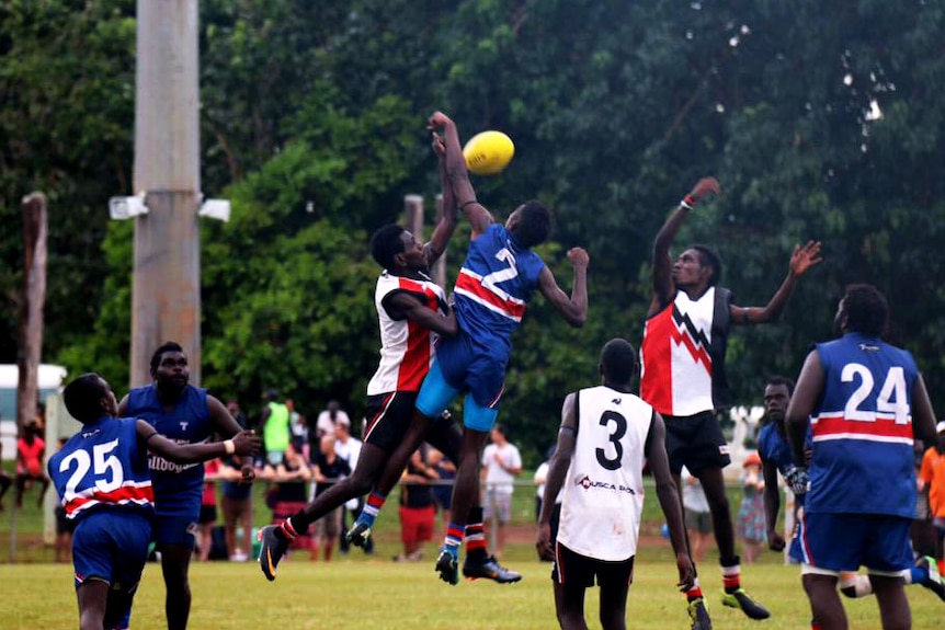 Two ruckmen jump for the ball on a football field.