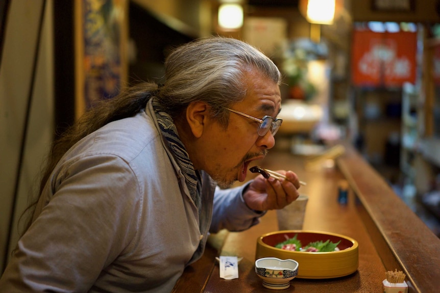 A man bringing a piece of whale meat to his mouth with chopsticks