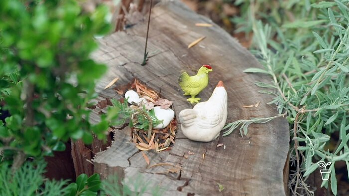 Two small chicken model toys sitting on a log in a garden