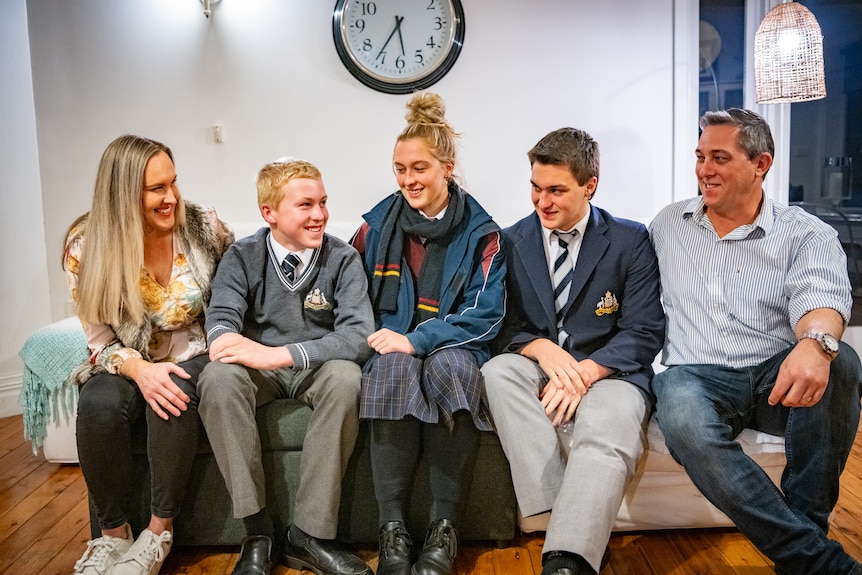 Knox's sitting on a couch laughing with his mum, sister, brother and father.