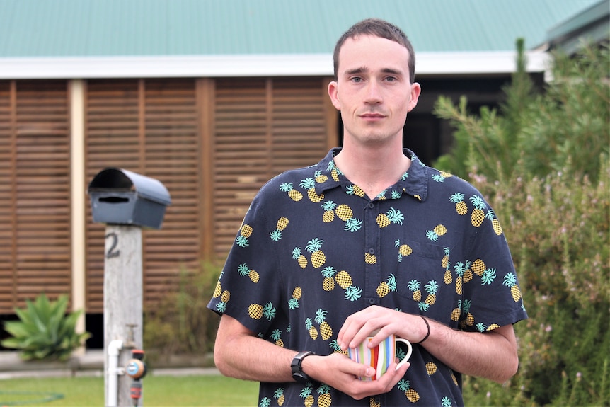 He wears a pineapple patterned shirt and stands near his letterbox