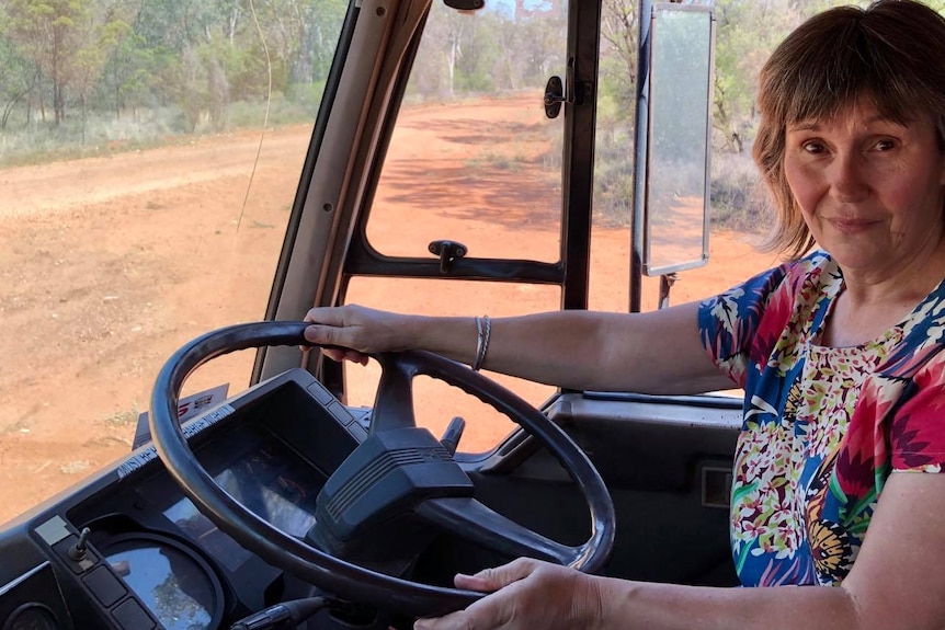 A woman sits behind the wheel of a truck on a dirt road