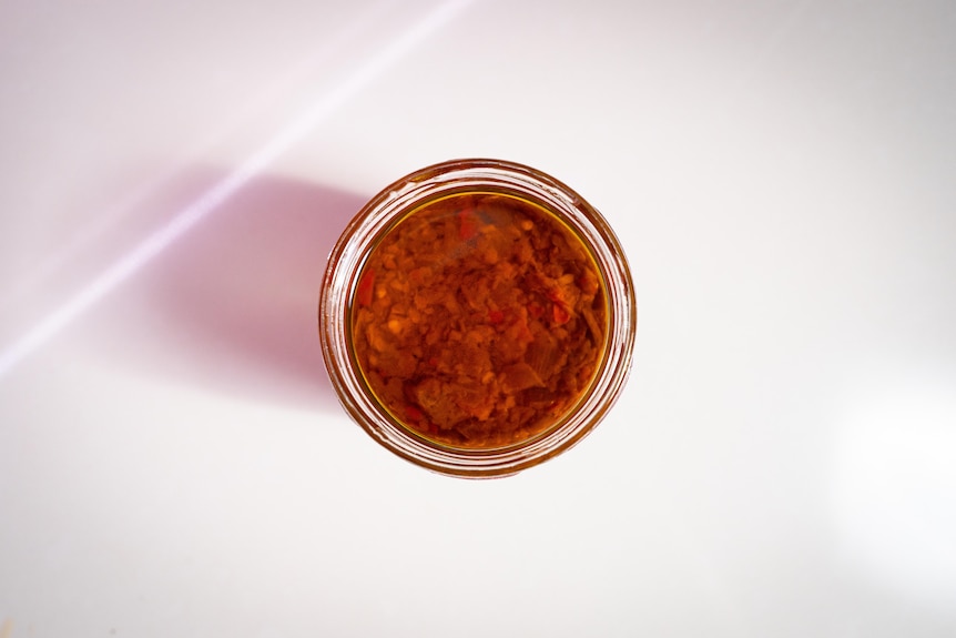 A bird's eye view photo of a red sauce in a jar.  It's on a white table.