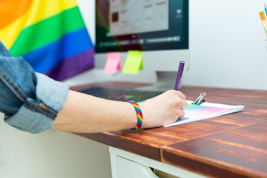 Anonymous woman at a desk with a rainbow flag on her desk and a rainbow bracelet on her wrist.