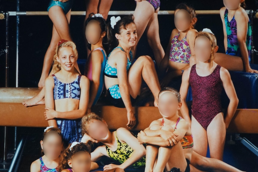 A group of young girls in leotards posing in front of gym apparatus.