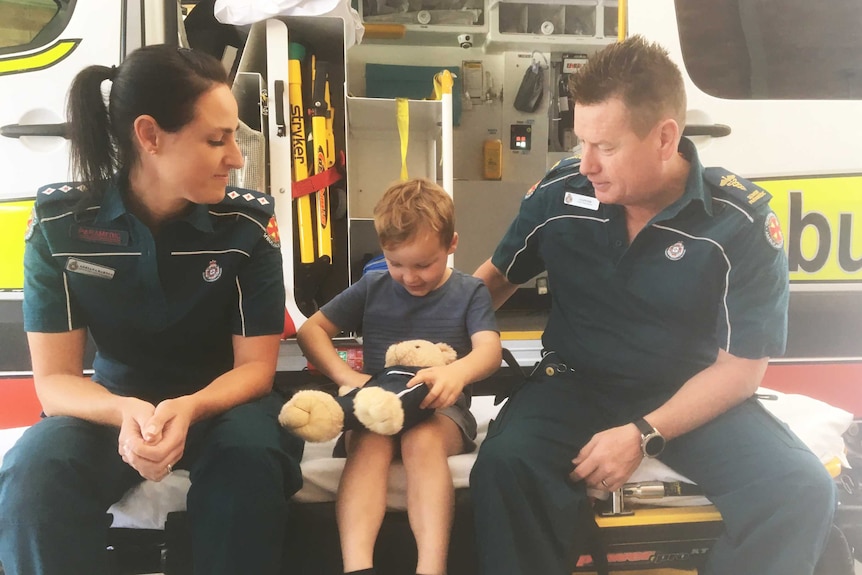 Thomas Skrypinsky sits on an ambulance stretcher two ambulance officers.