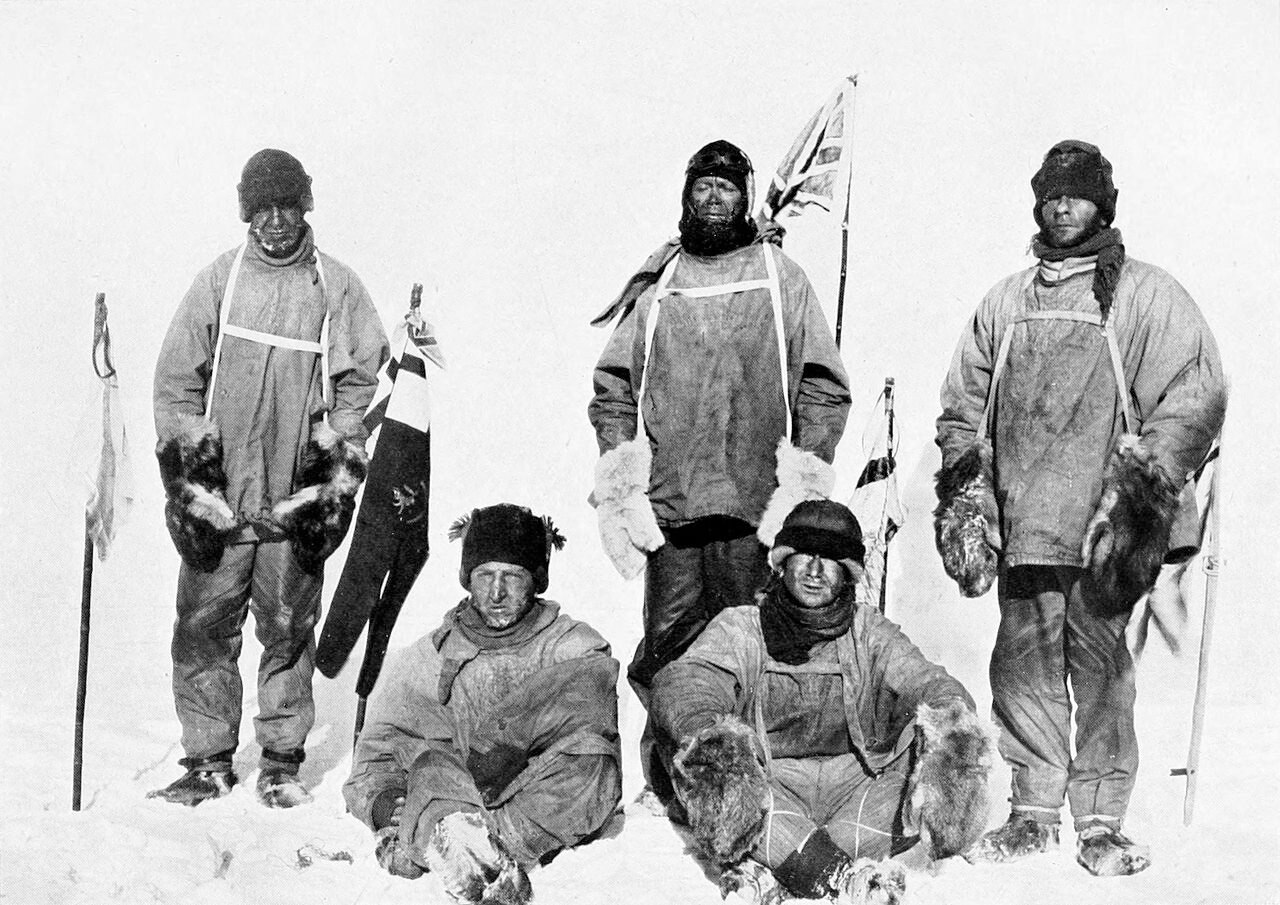 Black and white image of five men in thick clothes and hats standing in the snow