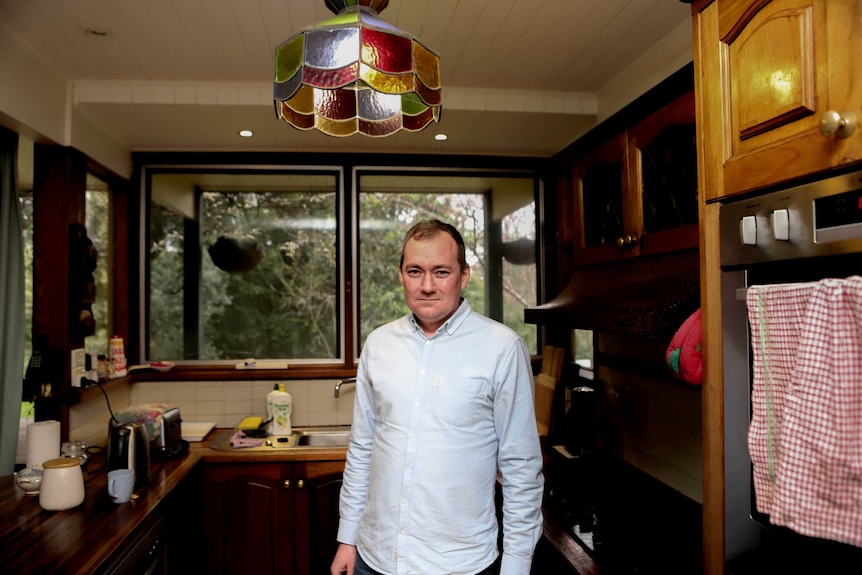 Man in blue shirt stands in kitchen under stained glass light fixture