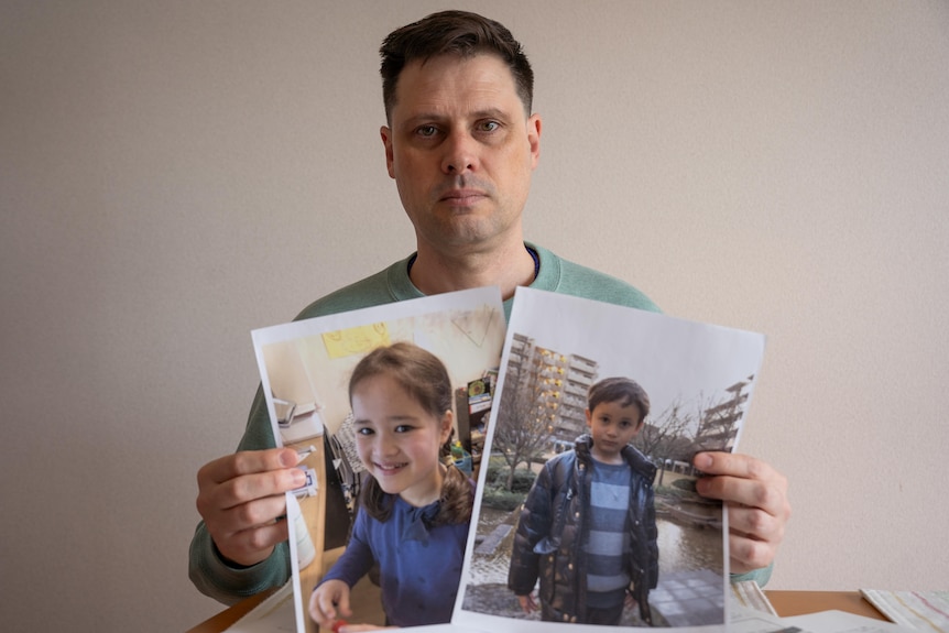 A man holding up photos of his daughter and son.