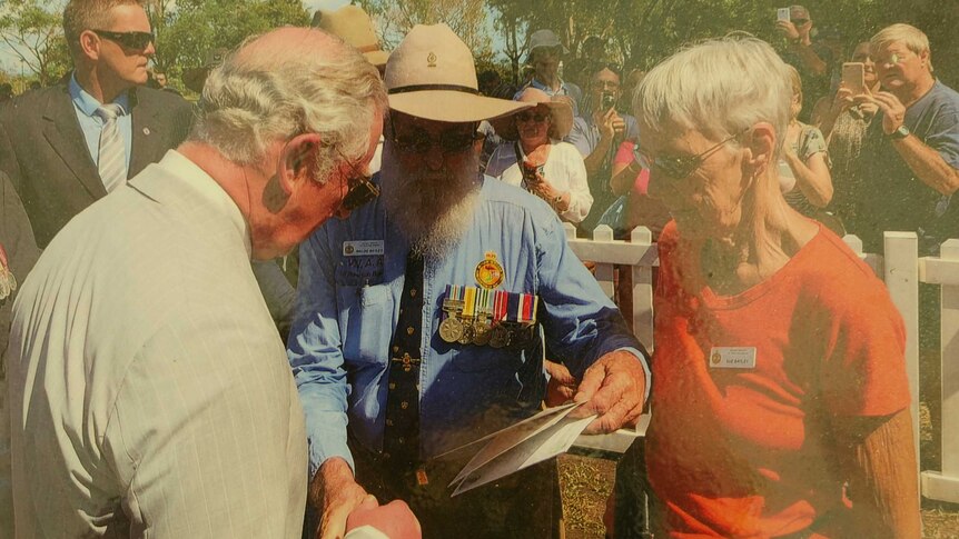 Prince Charles in Darwin in 2017 with older couple looking at poetry book.