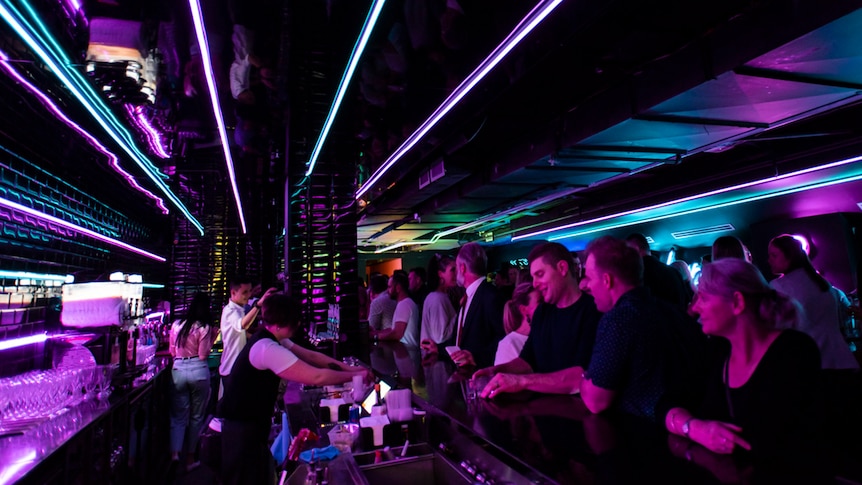 A crowded bar with neon lights and staff serving drinks to customers.