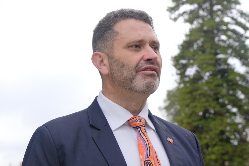 A man wearing a suit and colorful tie speaks to the media