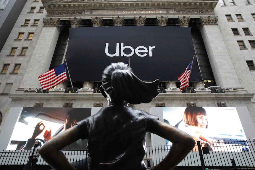 The statue of Fearless Girl stands in front of the New York Stock Exchange before an Uber sign.