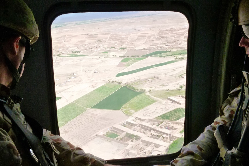 two uniformed soldiers look outside a Black Hawk helicopter above Oruzgan 