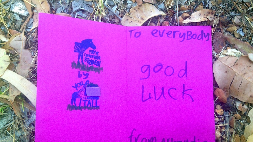 A card written by a child resting on ground with the words To Everybody Good Luck