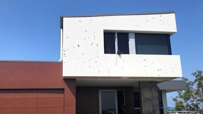 The exterior of a modern-looking home covered with spots where hail has ripped off paint.