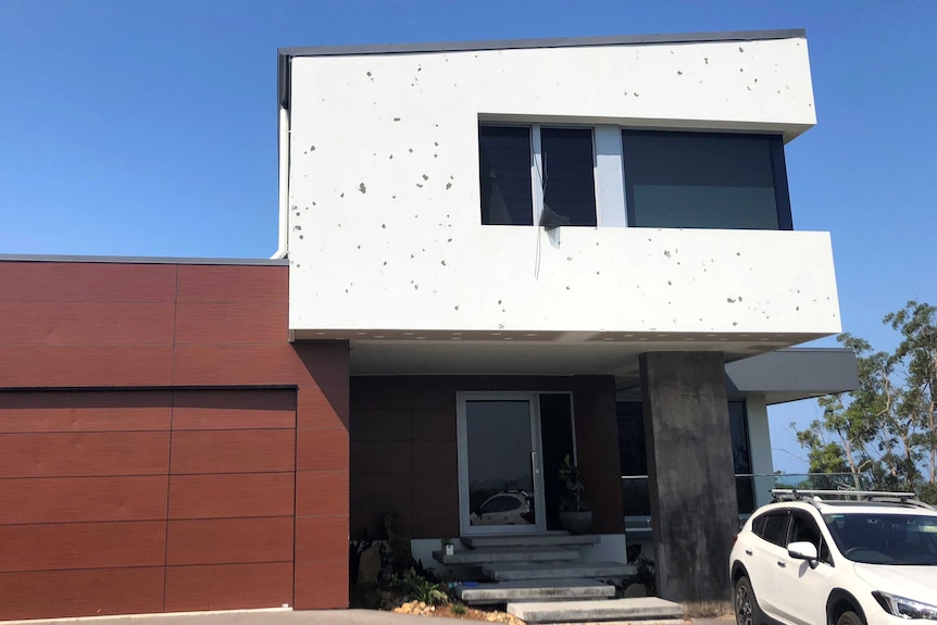The exterior of a modern-looking home covered with spots where hail has ripped off paint.