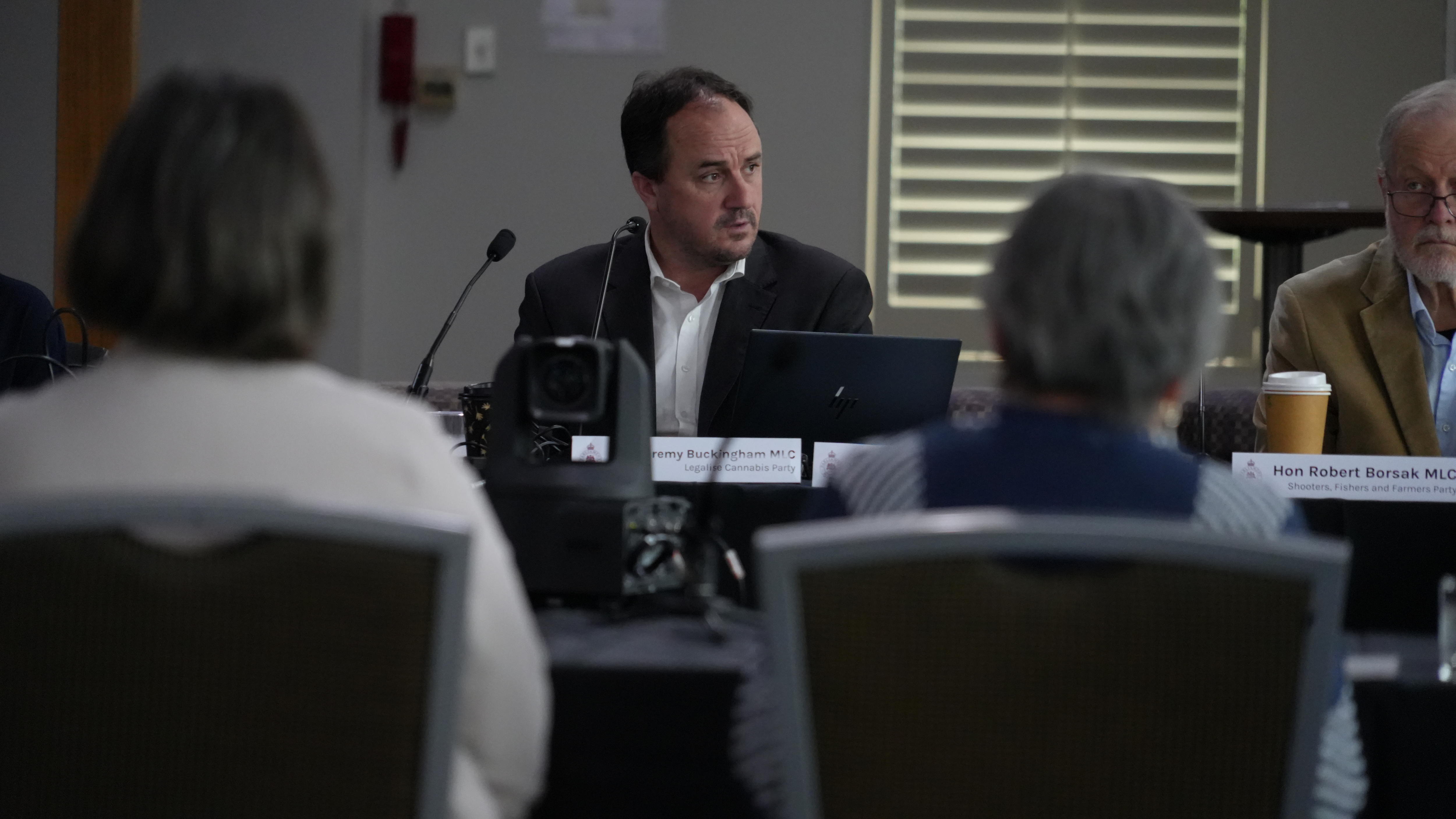 A man sitting at a desk  with computers and microphones in front of people.