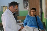 A doctor looks at a teenage boy's leg which is in a cast, his other has had the foot amputated