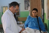 A doctor looks at a teenage boy's leg which is in a cast, his other has had the foot amputated