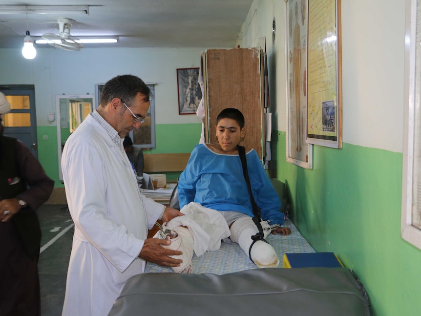 A doctor looks at a teenage boy's leg which is in a cast, his other has had the foot amputated