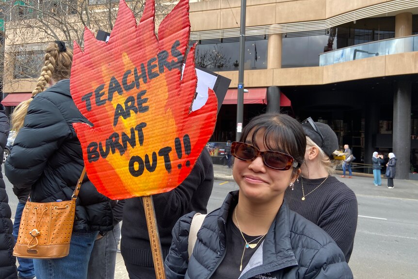 Person holds a sign saying 'Teachers are burnt out'