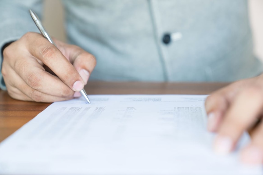 Hands of a person - one hand holding a pen - filling in a form sitting on a desk.