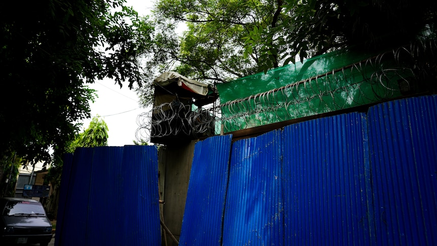 A makeshift tower sits just above a wall with barbed wire spiralled on top