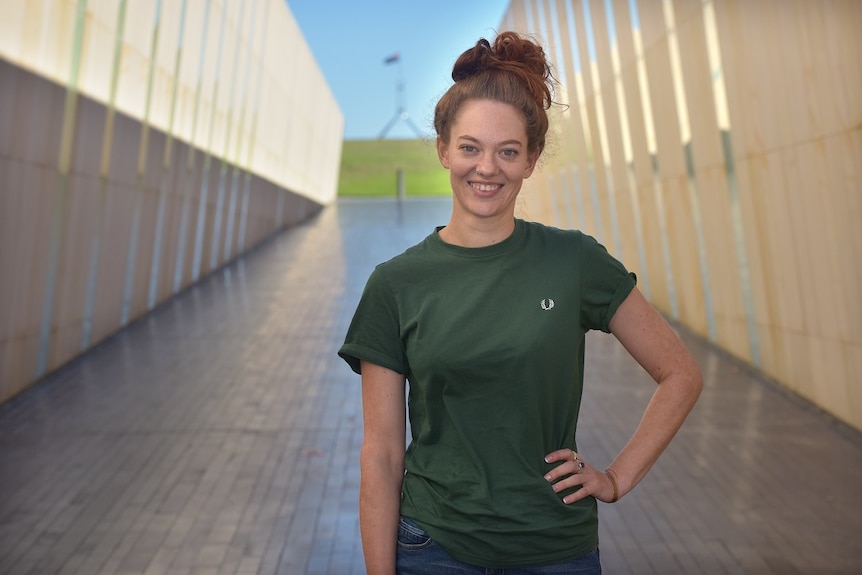 A woman in a green tshirt stands in a corridor in Canberra with Parliament House in the background