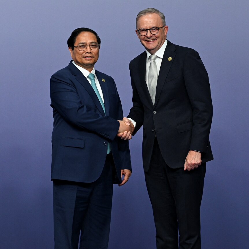 Vietnamese Prime minister Pham Minh Chinh and Antony Albanese shake hands and smile at the camera in front of a blue backdrop. 