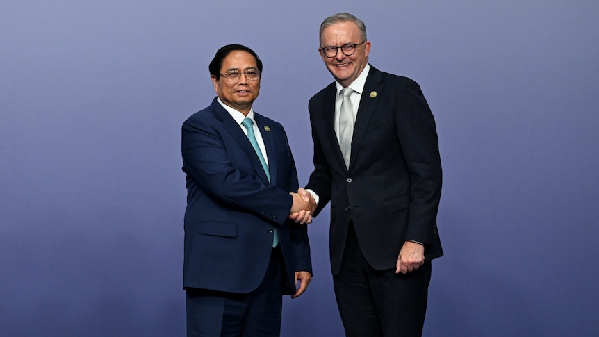 A shorter Asian man in a suits shakes hands with a smiling Anthony Albanese on a stage