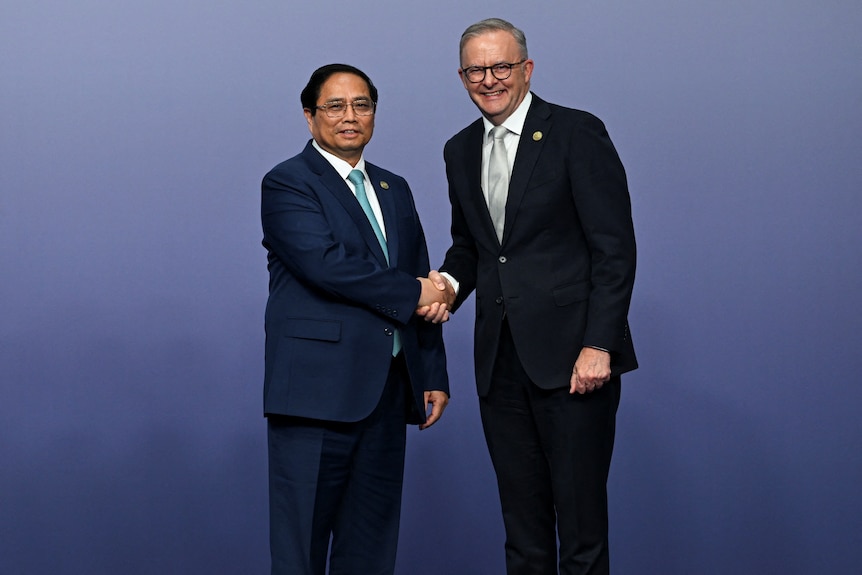 A shorter Asian man in a suits shakes hands with a smiling Anthony Albanese on a stage