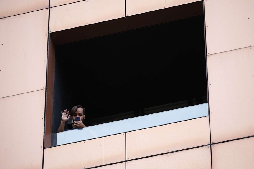 A man waves and is on the phone while in hotel quarantine at Peppers on Waymouth Street in Adelaide.