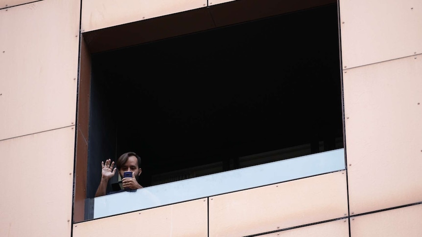 A man waves and is on the phone while in hotel quarantine at Peppers on Waymouth Street in Adelaide.