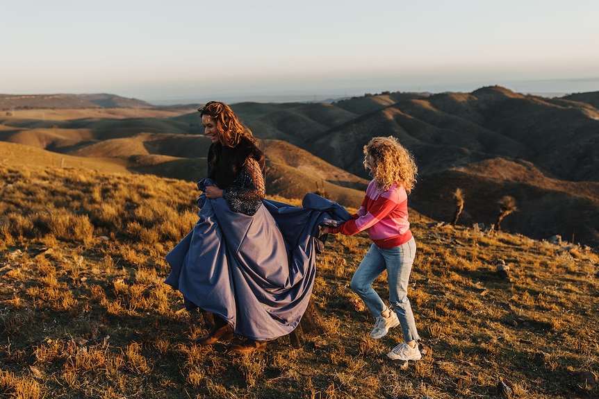 Photo of two women walking up a hillside, one is wearing a gown.