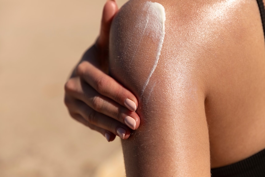 A person rubs sunscreen onto their shoulder.