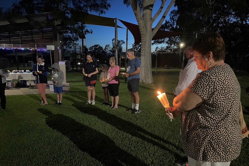 a wide photo of people in a circle holding candles in the pre-dawn