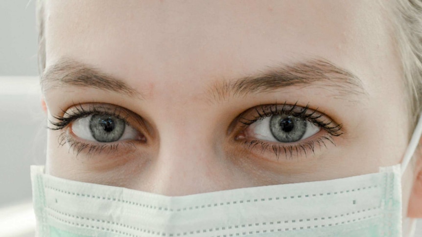 A close up of a woman's face. She's wearing a medical face mask
