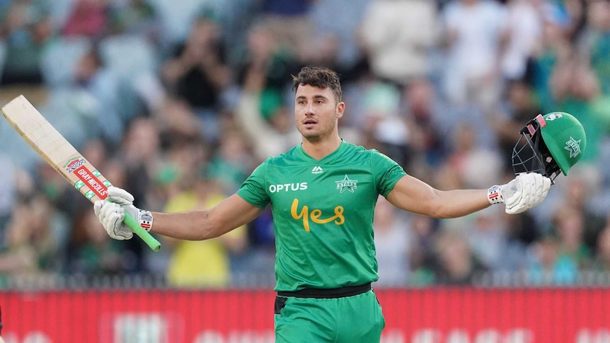 Marcus Stoinis holds his arms out wide with his bat in one hand and his helmet in the other