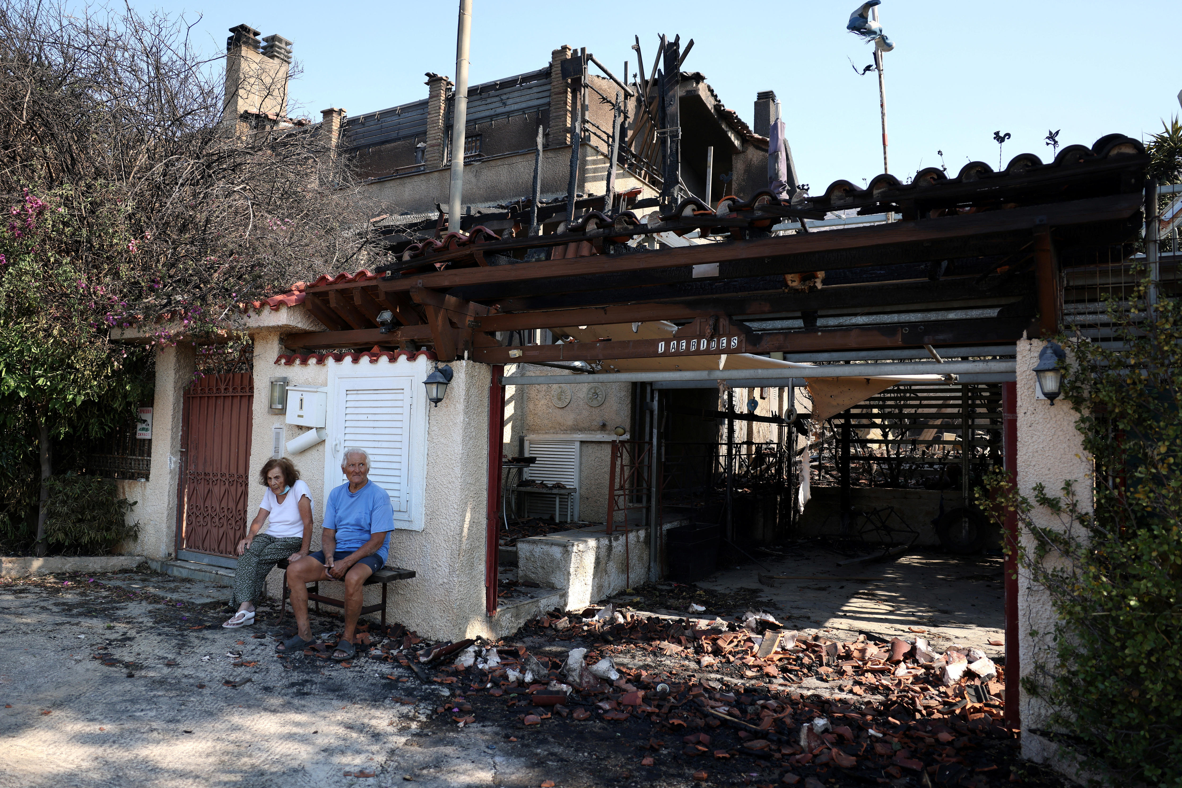 A couple sit on a bench outside a house which has been damaged by fire. 