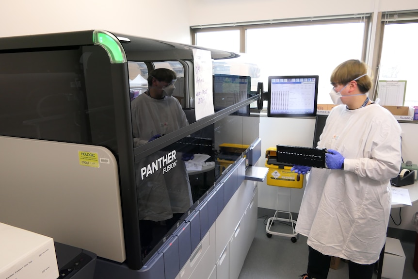 A lab technician standing next to a large black machine