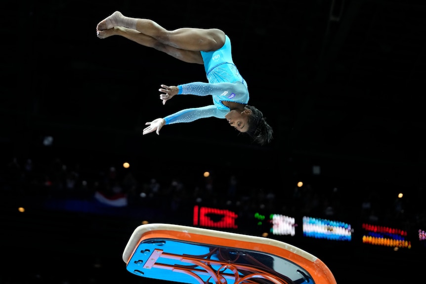 Simone flies over a vault with her arms and legs stretched out in front of her.