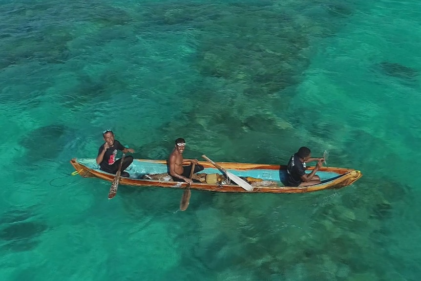 Three Indonesian men sit smiling in a small canoe in turquoise ocean