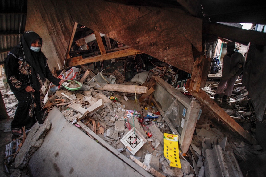 A woman walks through the rubble of a collapsed home.