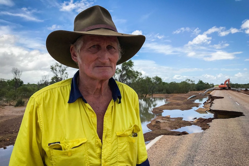 A man in a hi-vis work shirt wearing an Akubra, standing next to a damaged road.